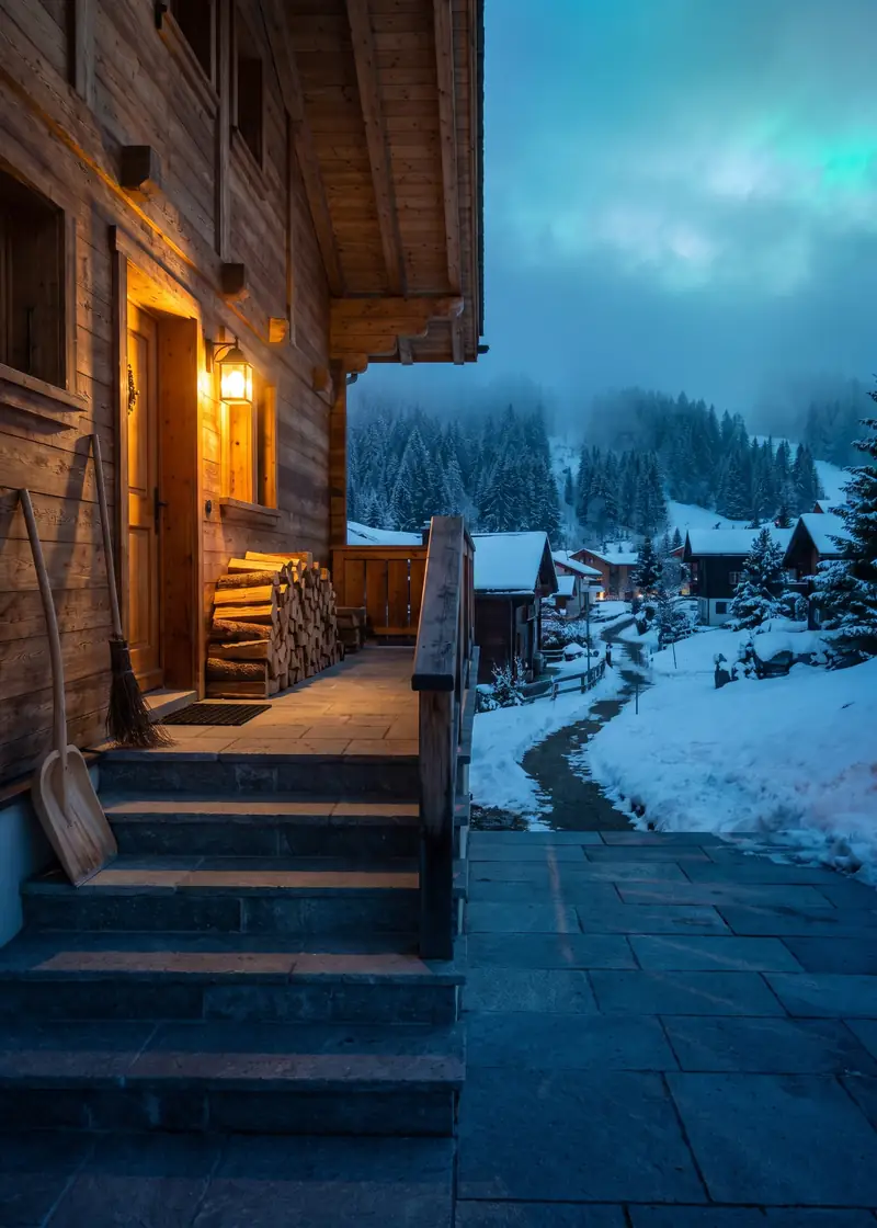 Hauswartung Klosters: gepflegter Eingang eines Holzchalets, dahinter die verschneiten Wälder von Klosters